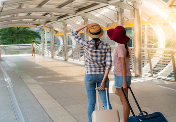 The back of two teenage girls who are friends, walking in the street or the walkway, holding carrying a suitcase, trolley wheel. To travel concept.