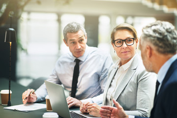 Three mature businesspeople having a meeting in an office lobby