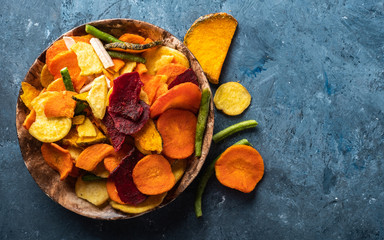 Dried vegetables chips from carrot, beet, parsnip and other vegetables on blue backgrounds. Organic diet and vegan food