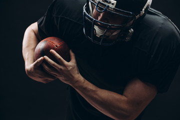 Wall Mural - Handsome caucasian man wearing american football uniform and helmet running in action with a ball over dark background