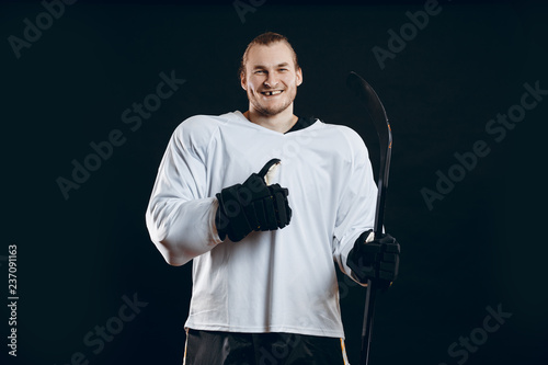Fototapeta na szkło Portret wesoły przystojny hokeista wpada w nastrój wygranej przed rozpoczęciem gry. Sportowiec ono uśmiecha się przy kamerą odizolowywającą na czerni w bielu mundurze