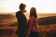 © Strelciuc - Back view of young man in stylish hat showing magnificent sunset sky to anonymous girlfriend while standing in meadow together.Unrecognizable guy pointing at sunset sky for girlfriend