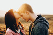 © Strelciuc - Side view of cute young female kissing handsome guy in forehead while standing in field together.Woman kissing boyfriend in forehead in nature