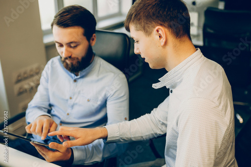 Fotografía Two handsome male colleagues interacting with tablet screen while sitting at office table together and working
