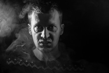 Wall Mural - Monochrome portrait of a man who is angry and has bad emotions with a face mash and smoke around on a black isolated background. The face of the guy in the shade with color illumination.