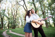 © soleg - young couple walking in the forest and playing guitar, summer nature, bright sunlight, shadows and green leaves, romantic feelings
