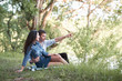 © soleg - young couple sitting on the grass in the forest and looking on sunset, summer nature, bright sunlight, shadows and green leaves, romantic feelings