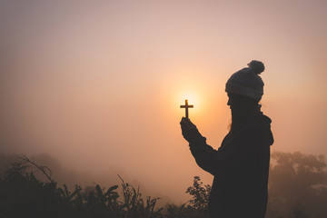 Wall Mural - Silhouette of christian young woman praying with a  cross at sunrise, Christian Religion concept background.