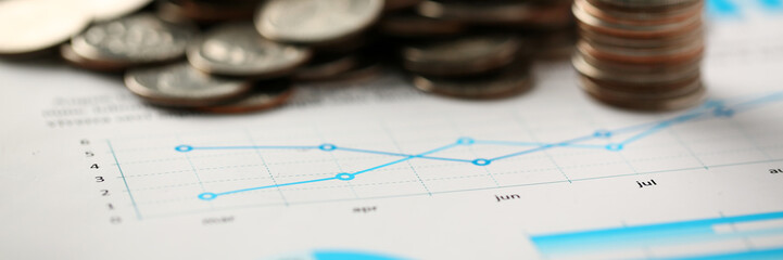 Pile of silver coins stand at financial graph papers