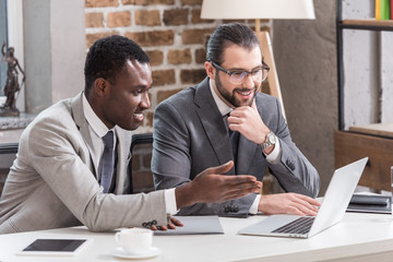 Wall Mural - multiethnic businessmen smiling and looking at laptop screen in office