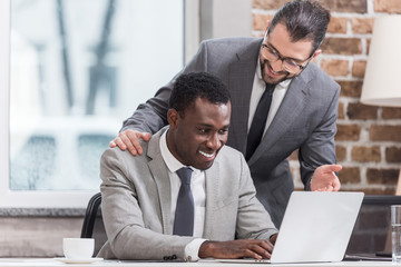 Wall Mural - african american businessman typing on laptop keyboard while smiling partner talking to him