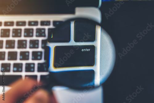 Fotografía The man's hand holds a magnifying glass that signifies the safe use of computers with the enter button