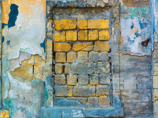 Wall Mural - Window opening laid with yellow stones in the old wall covered with many layers of colored stucco and partially destroyed under the influence of time and weather