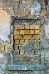 Wall Mural - Vertical photo of the window opening laid with yellow stones in the old wall covered with many layers of colored stucco and partially destroyed under the influence of time and weather