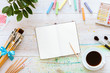 © insta_photos - Flat style artistic design workspace, blank notebook mock up for creative sketches with watercolor paints, pencil, set of paintbrushes and cup of coffee on white wooden table, top view, copy space
