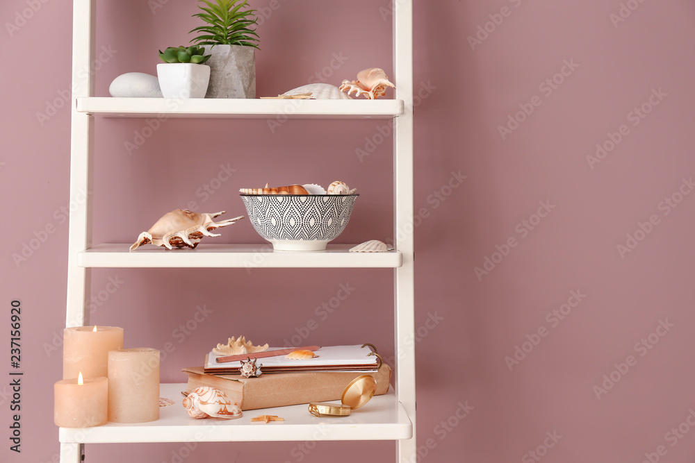 Shelving with sea shells, candles and other decorations near color wall