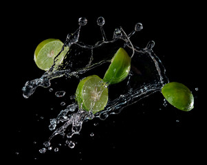 Wall Mural - limes with water splash or explosion flying in the air isolated on black background