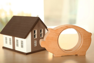 Poster - Piggy bank with house model on wooden table