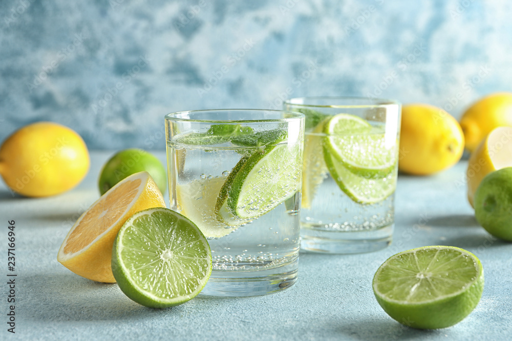 Glasses of water with lemon and lime on color table
