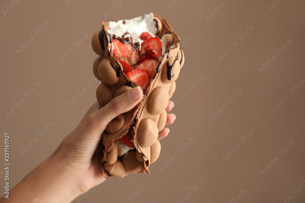 Female hand with delicious sweet bubble waffle on color background