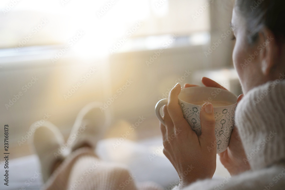 Cosy brunette at home on couch with hot drink - obrazy, fototapety, plakaty 