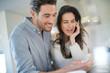 © goodluz - Stunning couple happily looking at cellphone in kitchen