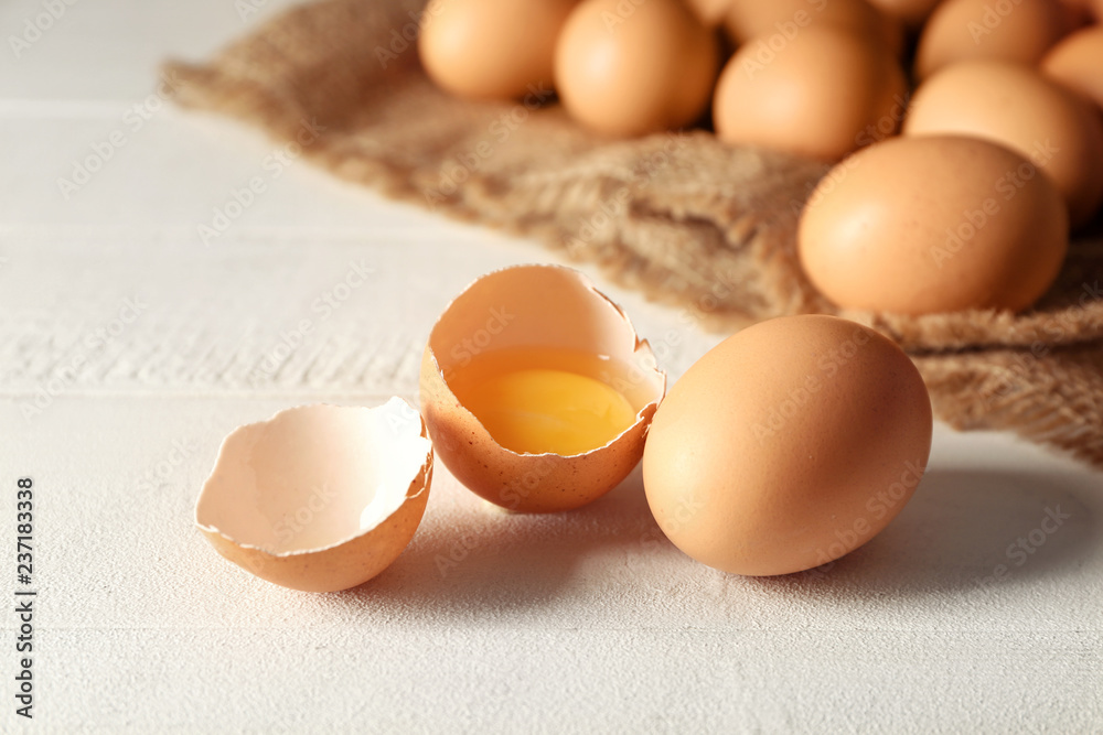Cracked and whole chicken eggs on white table