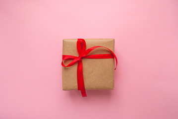 Wall Mural - Gift box wrapped in brown colored craft paper and tied with red bow on pink background.