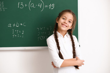 Cute girl standing near chalkboard in classroom