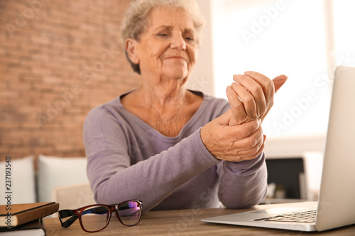 Fotografía Senior woman suffering from pain in wrist while sitting at table with laptop