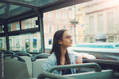 Foto A girl in glasses with long dark hair sits inside a tour bus and looks into the camera and looks out the window