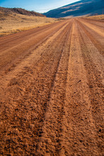 A Rural Dirt Road Recedes Into The Distance, Tire Tracks Leading To A Faraway Mountain