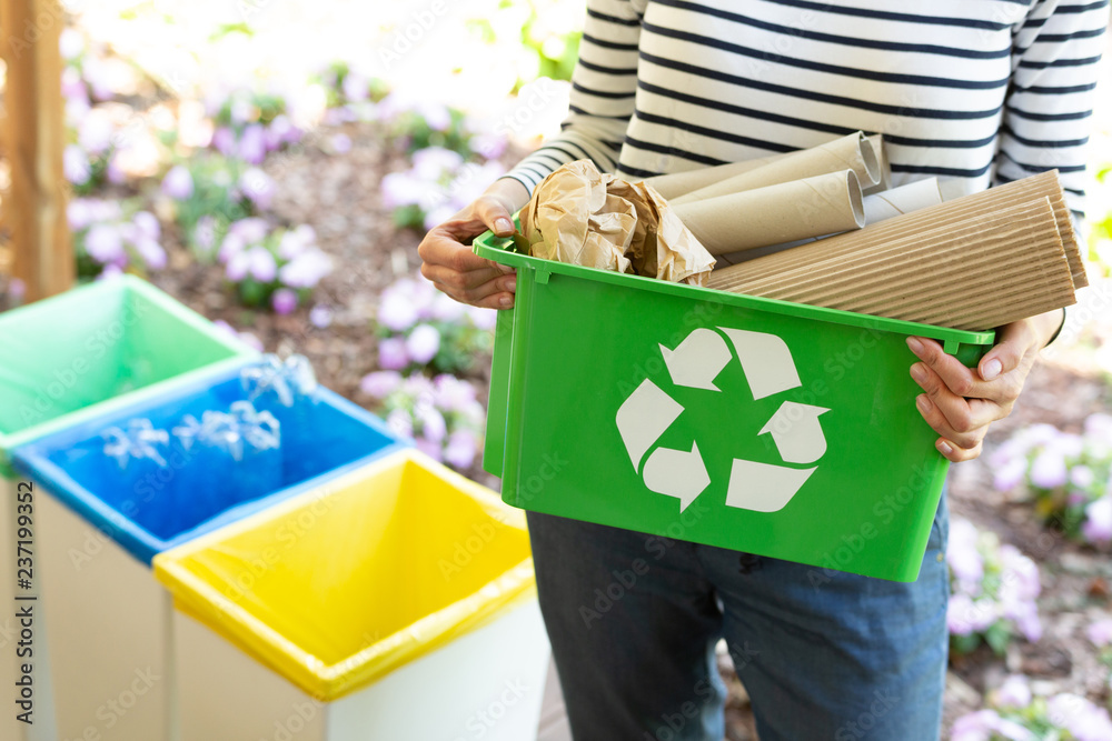 Close-up of a green basket with a recycling symbol with papers held by a woman - obrazy, fototapety, plakaty 