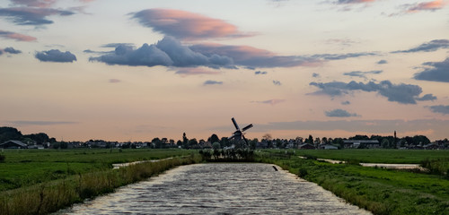 Wall Mural - canal in holland with an old windmill on the horizon below a colorful sky. traditional dutch scene, 