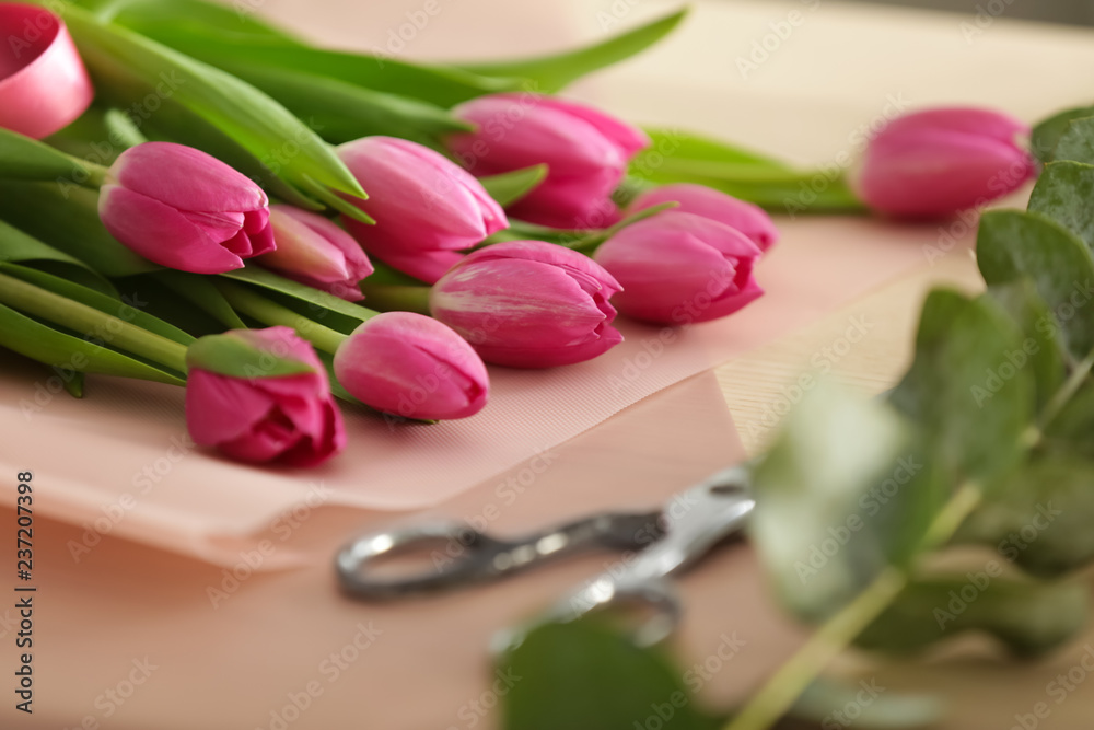 Beautiful tulips with scissors on table of florist