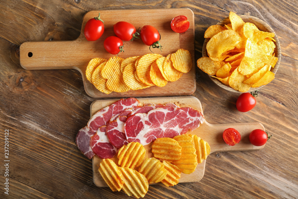 Tasty crispy potato chips with bacon and tomatoes on wooden table