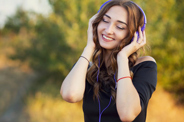 Wall Mural - portrait of a music lover teenager girl in headphones, young woman listening to lovely song on the nature in the field