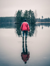 Man Is Walking On Water Ice Lake. Light Is Reflected Lika A Mirror. Small Island In Background.