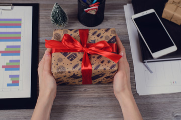 Pov high angle first person overhead view close up photo of beautiful red ribbon bow paper wrapped closed package unwrapped unpack in hands over wooden table