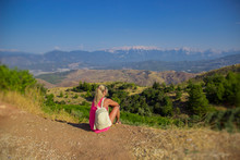 Young Woman Sitting At Edge Of Cliff Looking Over Expansive View Of Plains And Mountains.