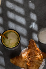 A cup of matcha latte art so delicious with croissants and milk jar on a beton background with hard light. flat lay.