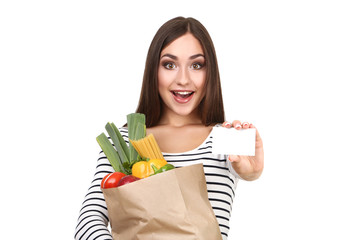 Wall Mural - Beautiful woman holding blank card and grocery shopping bag on white background