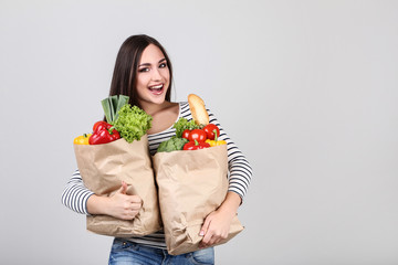 Wall Mural - Beautiful woman holding grocery shopping bags on grey background