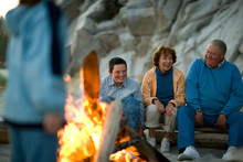 Mature Couple And Their Teenage Grandson Sitting Around A Bonfire On A Beach.