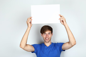 Beautiful young man holding blank board on grey background