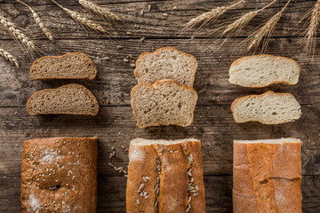 Wall Mural - Different fresh bread and spikelets of wheat on rustic wooden background. Creative layout made of bread. Healthy food concept, top view, flat lay, copy space