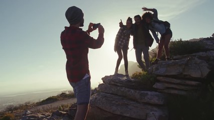 Wall Mural - young man taking picture of his friends standing on rocks during a hike. group of hikers taking phot