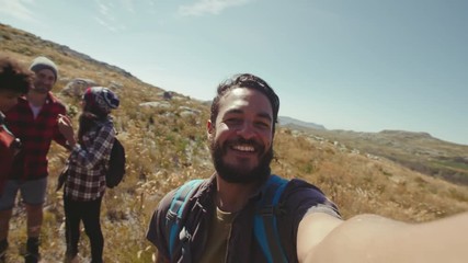 Wall Mural - Young man taking selfie with friends during a hike. Man filming funny moments of friends during a country walk.