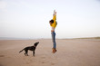 © Amsterdam/Stocksy - young woman with black dog on the beach, jumping