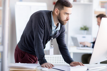 Side view portrait of bearded office worker using computer standing at desk, copy space